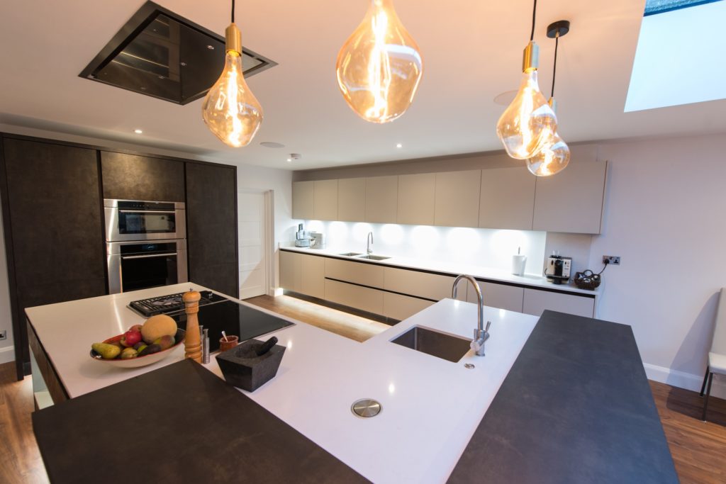 A kitchen island with hob and ceiling extractor and statement lighting.