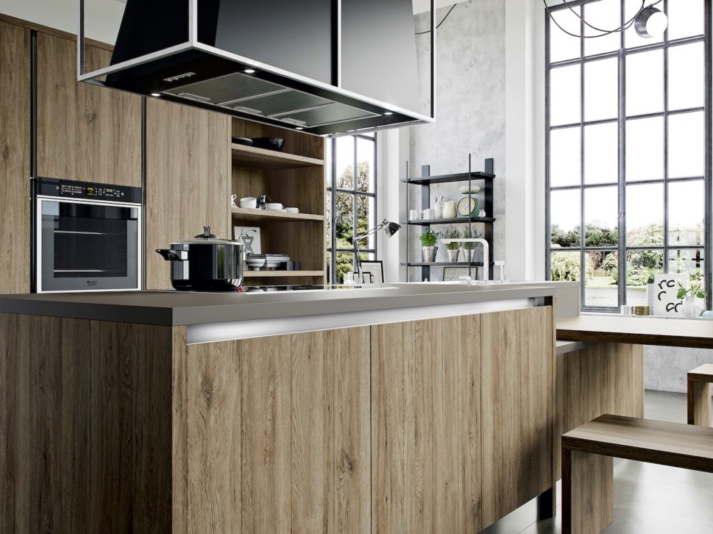 A hood extractor over a hob on an island. A contemporary kitchen with wood cabinets and breakfast bar.